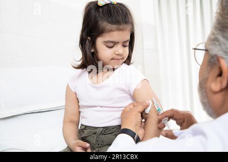 Un pédiatre indien senior effectue une vaccination d'une petite fille. Médecin administrant une injection à une femme enfant dans une clinique. Injection de syr Banque D'Images