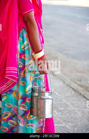 Vue partielle de la main d'une femme avec de nombreux bracelets, portant deux churns de lait dans la rue Banque D'Images