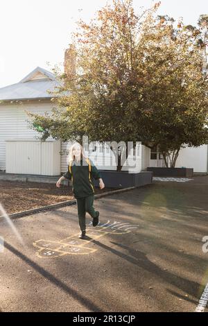 Une fille australienne de l'école primaire jouant le hopscotch dans la cour de l'école à l'évidement Banque D'Images