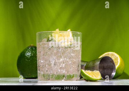 Cocktail d'alcool de punch Ti froid glacé, petit punch, boisson mélangée à base de rhum avec garniture de tranche de citron vert frais, sur fond vert coloré Banque D'Images