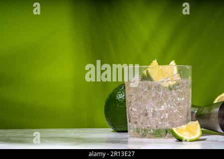 Cocktail d'alcool de punch Ti froid glacé, petit punch, boisson mélangée à base de rhum avec garniture de tranche de citron vert frais, sur fond vert coloré Banque D'Images