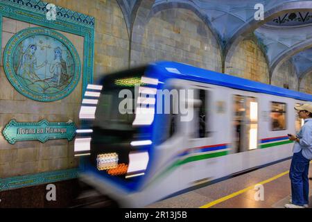 photo à l'obturateur lent du train en mouvement arrivant à la station de métro alisher navoi à tachkent, devant l'un des panneaux représentant l'une de ses histoires Banque D'Images