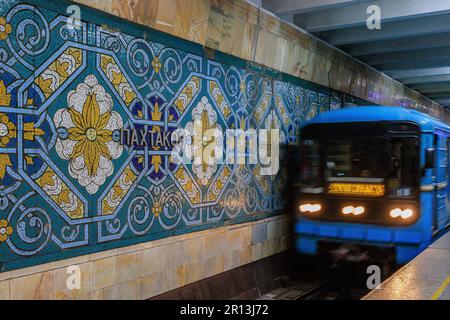photo à obturation lente d'un train légèrement flou arrivant à la station de métro pakhtakor aux motifs vifs célébrant l'industrie de la cueillette du coton Banque D'Images
