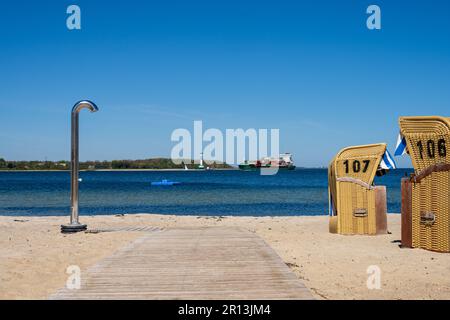 Heikendorf, Deutschland, Mai 2023 Sandstrand mit Strandkörben und einer Dusche, im Hintergund die Kiler Außenförde mit dem Leuchtturm und einem contai Banque D'Images