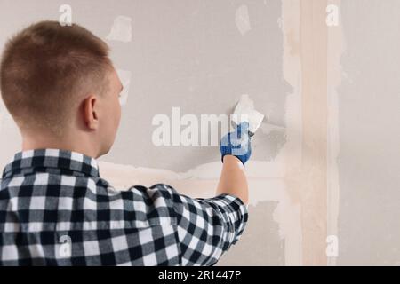 Homme plâtrage mur avec couteau à mastiquer à l'intérieur, vue arrière. Rénovation de la maison Banque D'Images