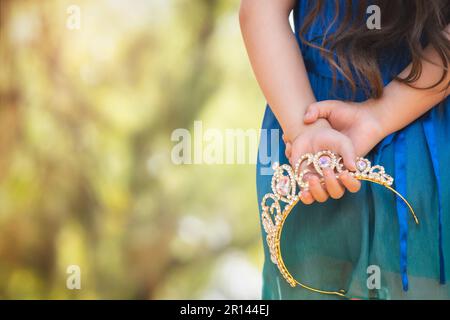 belle petite fille heureuse avec couronne jouant dans le parc en robe bleue sans chaussures riant criant avec bonheur en famille appréciant les enfants Banque D'Images