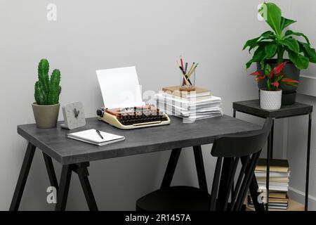 Machine à écrire et pile de papier sur table sombre dans la chambre. Lieu de travail du rédacteur Banque D'Images