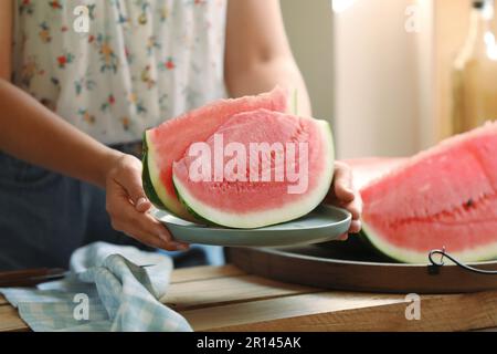 Femme tenant une assiette avec une coupe de pastèque fraîche juteuse sur une table en bois, gros plan Banque D'Images