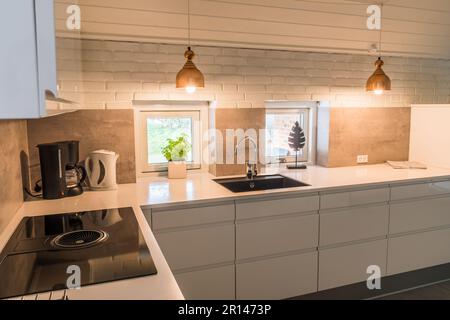 Kitchenette moderne avec plan de travail blanc, évier noir et lampes en métal cuivré de style industriel Banque D'Images