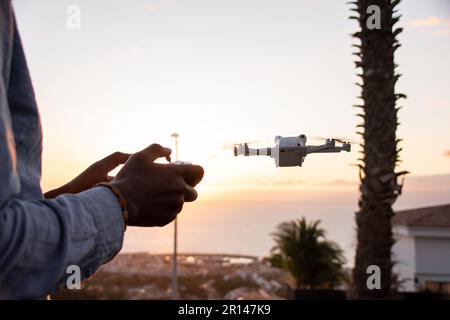 Gros plan sur les mains d'un homme afro-américain contrôlant son drone au coucher du soleil dans un endroit tropical Banque D'Images