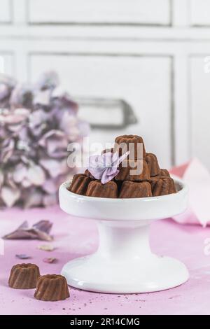 Pralines au chocolat sous forme de petits gâteaux Bundt, saupoudrés de cacao, sur fond rose clair, ornés de fleurs d'hortensia, verticales Banque D'Images