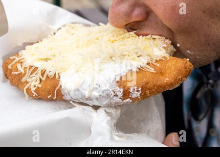 Un homme mangeant un langoush traditionnel, une pâtisserie frite populaire en Europe de l'est, servi avec des garnitures telles que le fromage et le yaourt, Street food, la popula Banque D'Images