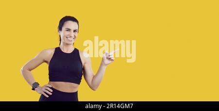 Joyeuse femme annonce des articles de sport et attire votre attention à copier l'espace sur fond jaune. Banque D'Images