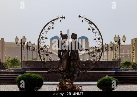 une statue de silhouette de deux figures avec une guirlande entoure la vue du minaret de l'islam khoja et les portes de la ville fortifiée de khiva ouzbékistan Banque D'Images