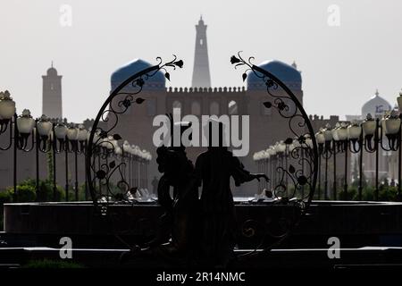 une statue de silhouette de deux figures avec une guirlande entoure la vue du minaret de l'islam khoja et les portes de la ville fortifiée de khiva ouzbékistan Banque D'Images