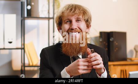 Un jeune homme d'affaires plein de confiance avec des lunettes regardant l'appareil photo avec le sourire sur le bureau à domicile. Portrait de face de redhead travailleur indépendant entrepreneur, chef d'entreprise patron homme Banque D'Images