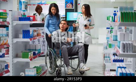 Jeune homme en fauteuil roulant parlant au pharmacien de médicaments, demandant un traitement sur ordonnance ou un médicament. Personne handicapée et gardien recevant des suppléments et des vitamines en pharmacie. Banque D'Images