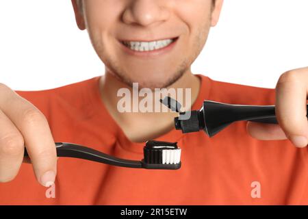 Homme appliquant du dentifrice au charbon de bois sur une brosse à dents sur fond blanc, gros plan Banque D'Images