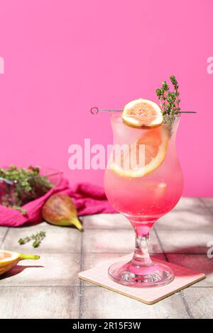 Cocktail d'été frais avec figues, pamplemousse et thym sur une table de carrelage près du mur rose Banque D'Images