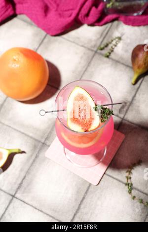 Cocktail d'été frais avec figues, pamplemousse et thym sur une table carrelée Banque D'Images