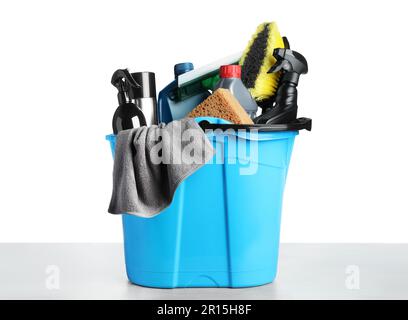 Seau avec de nombreux produits de lavage de voiture différents sur table grise sur fond blanc Banque D'Images