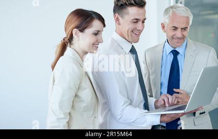 Ces derniers chiffres sont excellents. un groupe de collègues parlant autour d'un ordinateur portable dans un bureau. Banque D'Images