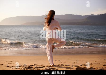 Vivre sur le son de la paix. une jeune femme faisant du yoga à la plage. Banque D'Images