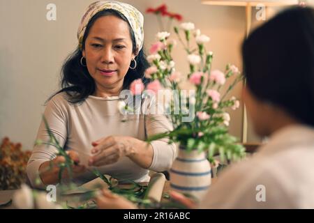 Attrayante femme asiatique à la retraite aime organiser un vase avec des fleurs fraîches dans un atelier. Concepts de loisirs et de loisirs Banque D'Images