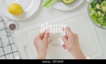 Recette de salade verte. Femme en train de préparer une vinaigrette. Gros plan des ingrédients sur fond blanc, plat Banque D'Images