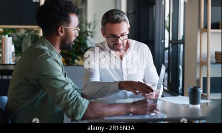 Le travail vient d'abord avec ces deux. deux hommes d'affaires utilisant un ordinateur portable et ayant une discussion dans un bureau moderne. Banque D'Images