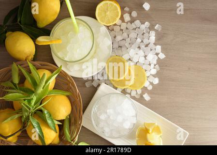 Limonade avec glace dans un verre sur un banc de cuisine en bois et panier avec des fruits et de la glace pilée autour. Vue de dessus. Composition horizontale. Banque D'Images
