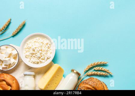 Happy Shavuot - concept religieux de vacances juives avec produits laitiers, fromage, pain traditionnel, bouteilles de lait, blé sur fond bleu, espace copie. Banque D'Images