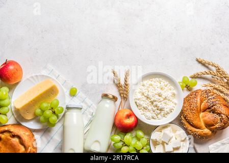 Happy Shavuot - concept religieux de vacances juives avec produits laitiers, fromage, pain, bouteilles de lait, blé et raisins sur fond blanc, espace de copie. Banque D'Images