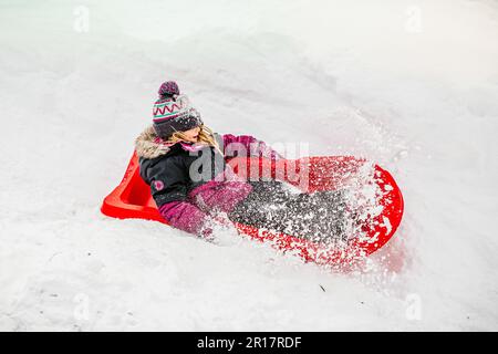 girld de 5 ans glissant sur un traîneau rouge lors d'une journée d'hiver Banque D'Images