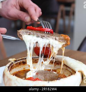 Gros plan d'un homme tenant une fourchette, tirant une tranche de viande recouverte de fromage mozzarella en fusion Banque D'Images