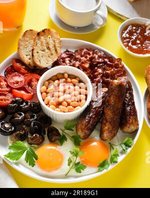 Petit-déjeuner anglais complet avec œufs frits, bacon, saucisses, haricots et champignons sur fond jaune. Banque D'Images