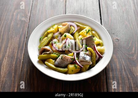 Salade de hareng avec pommes de terre bouillies, concombres marinés et oignon rouge dans un bol sur fond de bois. Vue rapprochée Banque D'Images