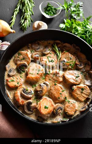 Médaillons de porc avec sauce aux champignons dans une casserole en fonte sur fond de pierre sombre. Vue rapprochée Banque D'Images