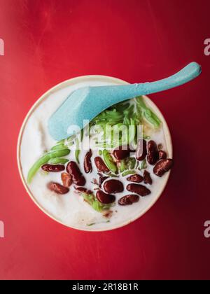 Un dessert malaisien sucré glacé traditionnel Cendol servi dans un bol avec du lait de coco et des haricots rouges. Banque D'Images