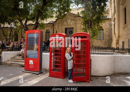 Valetta, Malte - 19 avril 2023: Femme posant pour la photo entre deux téléphones rouges britanniques dans la vieille ville historique. Banque D'Images