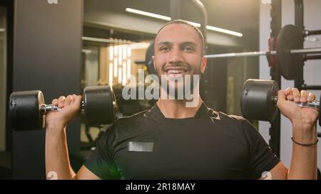 Joyeux souriant sportif afro-américain faisant de l'exercice de puissance à la salle de gym avec l'équipement de sport bodybuilder homme levant poids lourds haltères séance d'entraînement mâle Banque D'Images