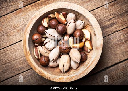 Fruits à coque mélangés séchés dans un bol en bois. Noix de macadamia, noix de pécan et noix du Brésil avec couteau sur table en bois. Prise de vue macro en studio. Photographie alimentaire Banque D'Images