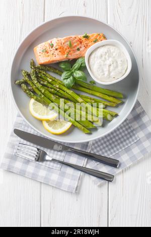Aliments sains filet de saumon cuit avec asperges servi avec une sauce tartare et un gros plan de citron dans une assiette sur la table. Vue verticale du dessus Banque D'Images