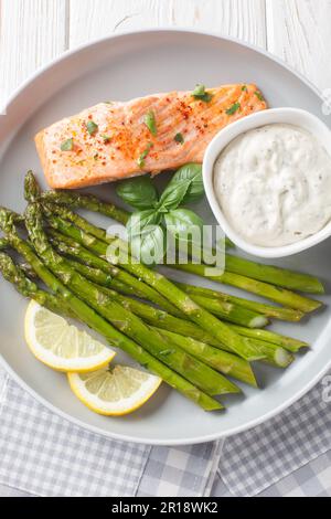 Filet de saumon cuit avec des asperges croustillantes servi avec de la sauce tartare dans une assiette sur la table. Vue verticale du dessus Banque D'Images