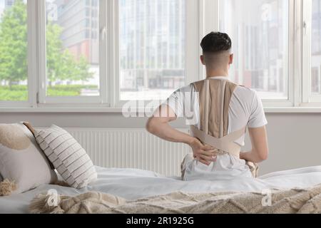 Homme avec corset orthopédique assis dans la chambre, vue arrière Banque D'Images