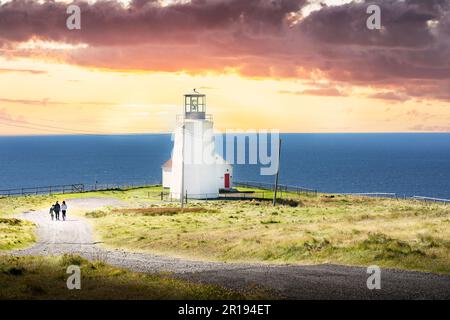 Coucher du soleil groupe de touristes marchant le long d'une route de gravier vers un phare le long de la côte est canadienne à Cape St. Mary's Terre-Neuve Canada. Banque D'Images