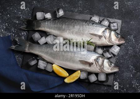 Poisson-bar frais cru, cubes de glace et quartiers de citron sur table noire, plat Banque D'Images