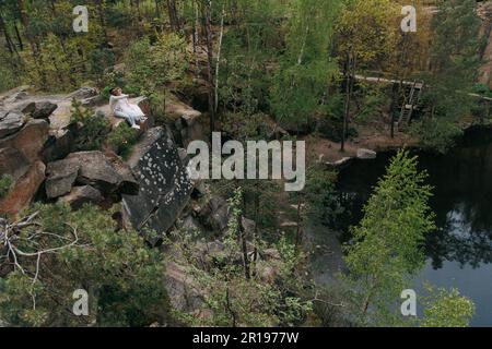 Jeunes couples interraciaux newlyweds se trouve sur le rocher et parle sur fond de forêt, de lac et de canyon. Concept de relations d'amour et d'unité betwe Banque D'Images