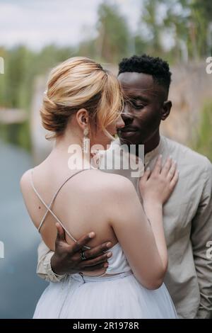 Heureux couple interracial newlyweds se tient et embrasse contre le fond de paysage magnifique. Concept de relations d'amour et d'unité entre diff Banque D'Images