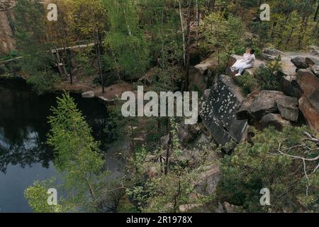 Jeunes couples interraciaux newlyweds se trouve sur le rocher et parle sur fond de forêt, de lac et de canyon. Concept de relations d'amour et d'unité betwe Banque D'Images